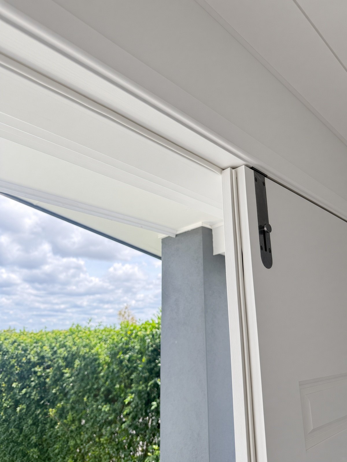 White bulb seal fitted along a door frame, looking out to a green hedge